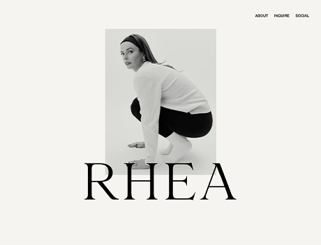 Whissel Strategies A woman in a white sweater and black pants squats on a platform, looking over her shoulder. The word "RHEA" is displayed in large text below her image, highlighting Whissel Strategies—a premier Toronto Marketing Agency. Toronto Digital Marketing Agency