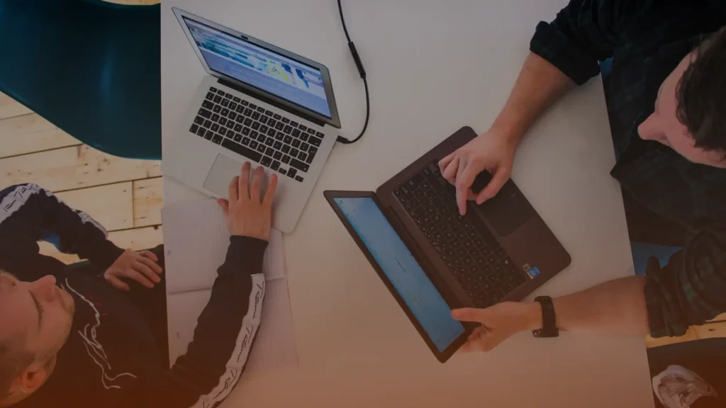 Whissel Strategies Two people work at a white table with open laptops, one person using a notebook and the other pointing at their laptop screen. Toronto Digital Marketing Agency