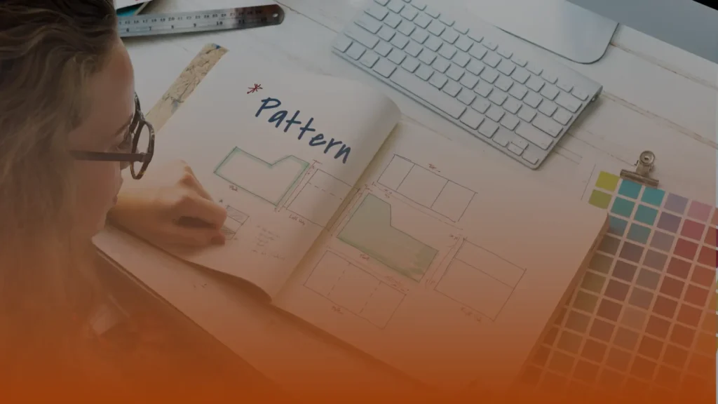 Whissel Strategies A person reviews a pattern design sketchbook with technical drawings, sitting at a desk with a keyboard, color swatches, and ruler. Toronto Digital Marketing Agency