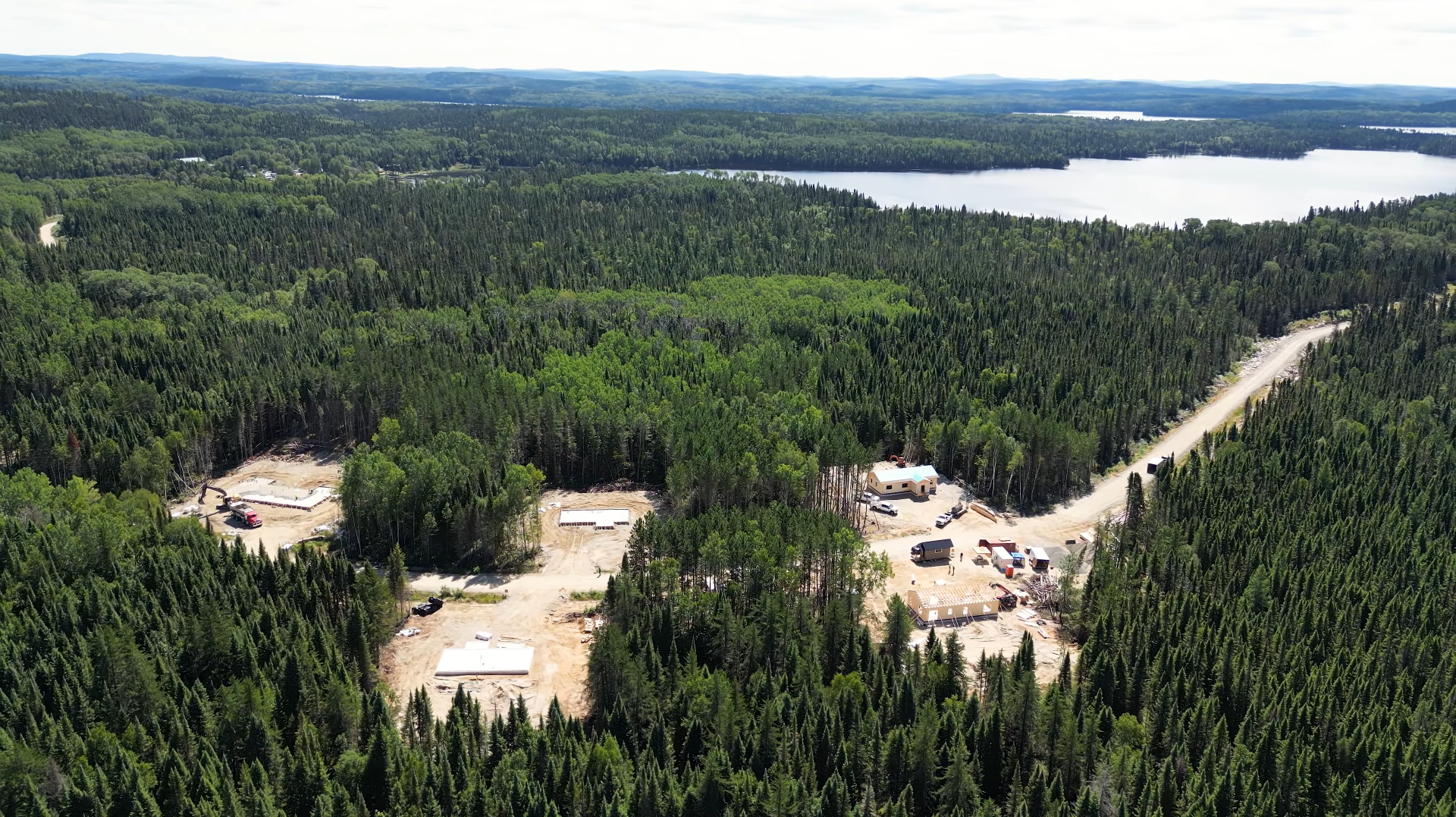 Whissel Strategies Aerial view of a construction site with several cleared areas and buildings surrounded by dense forest, with a lake visible in the background. Toronto Digital Marketing Agency
